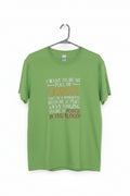 A bright green short-sleeve t-shirt hanging on a black metal hanger against a plain wall. The shirt features a humorous parody graphic with white and orange-red text that reads, 'I WANT TO BE SO FULL OF CHRIST THAT IF A MOSQUITO BITS ME IT FLYS AWAY SINGING THERE IS NO POWER IN THE BLOOD!'.